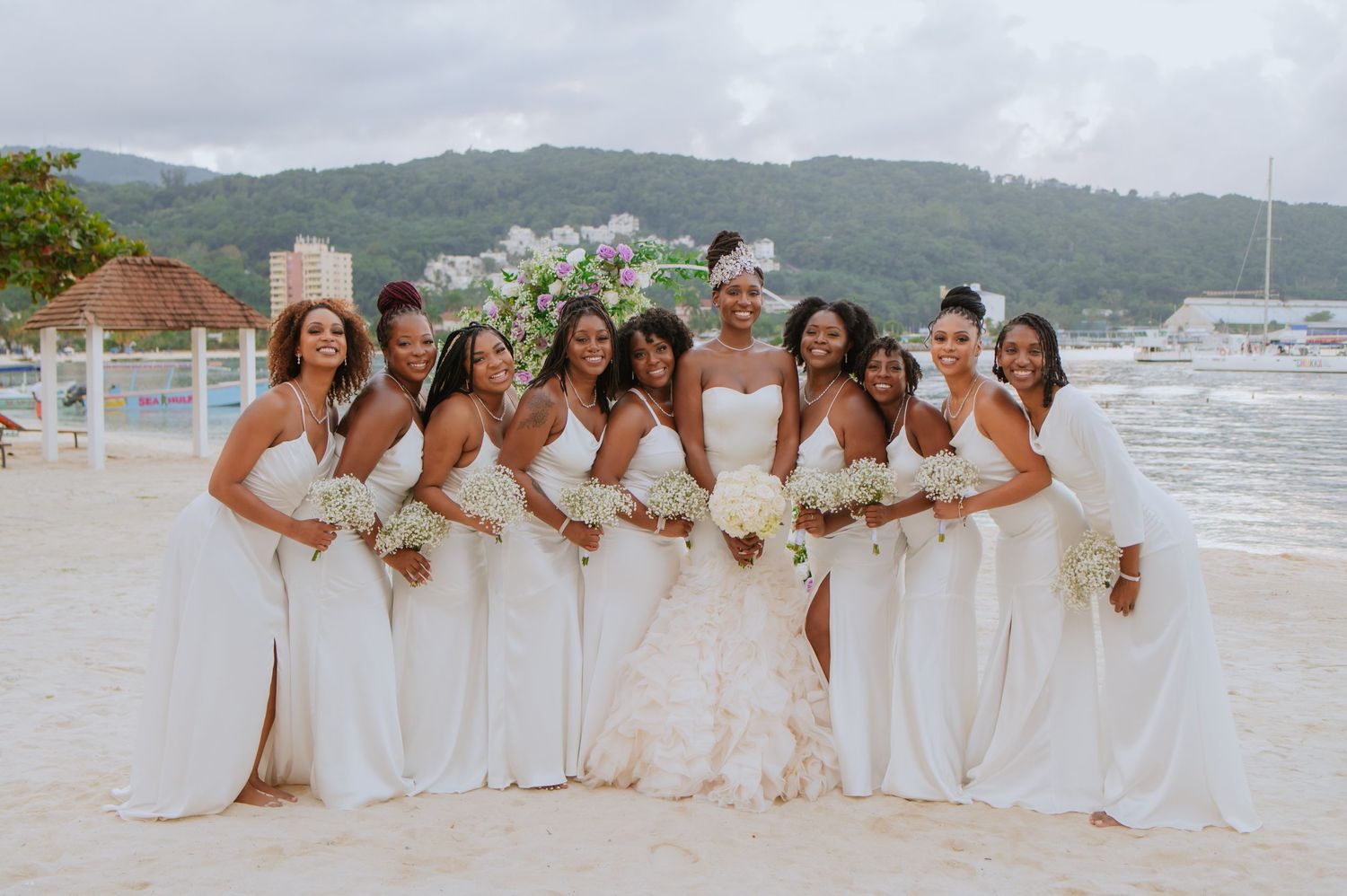 Bridal party in white dresses celebrating on a tropical beach.