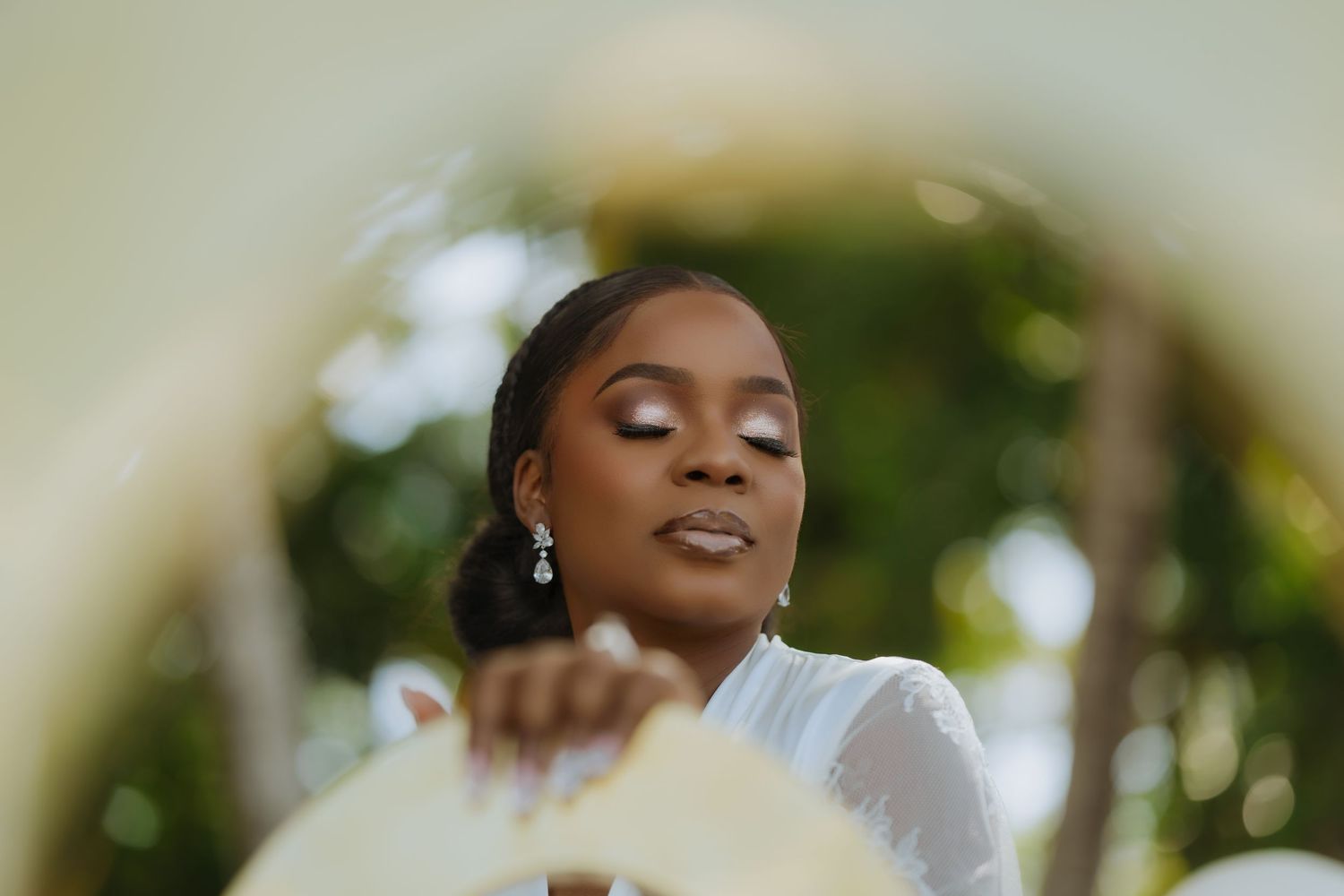 A bride wearing elegant jewelry and a white gown smiles during an outdoor wedding ceremony.