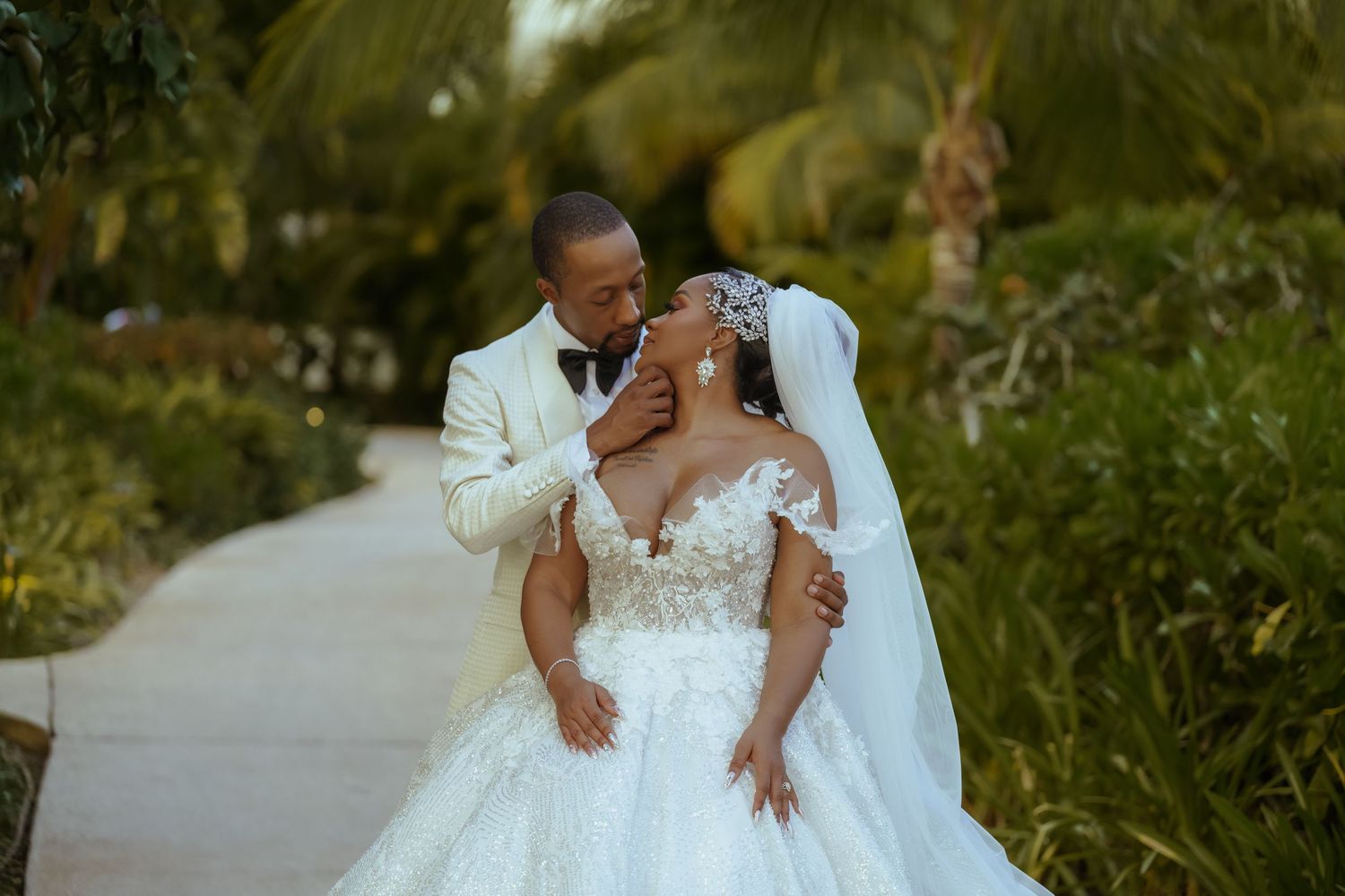 A romantic wedding couple embraces in an outdoor garden setting with lush greenery.