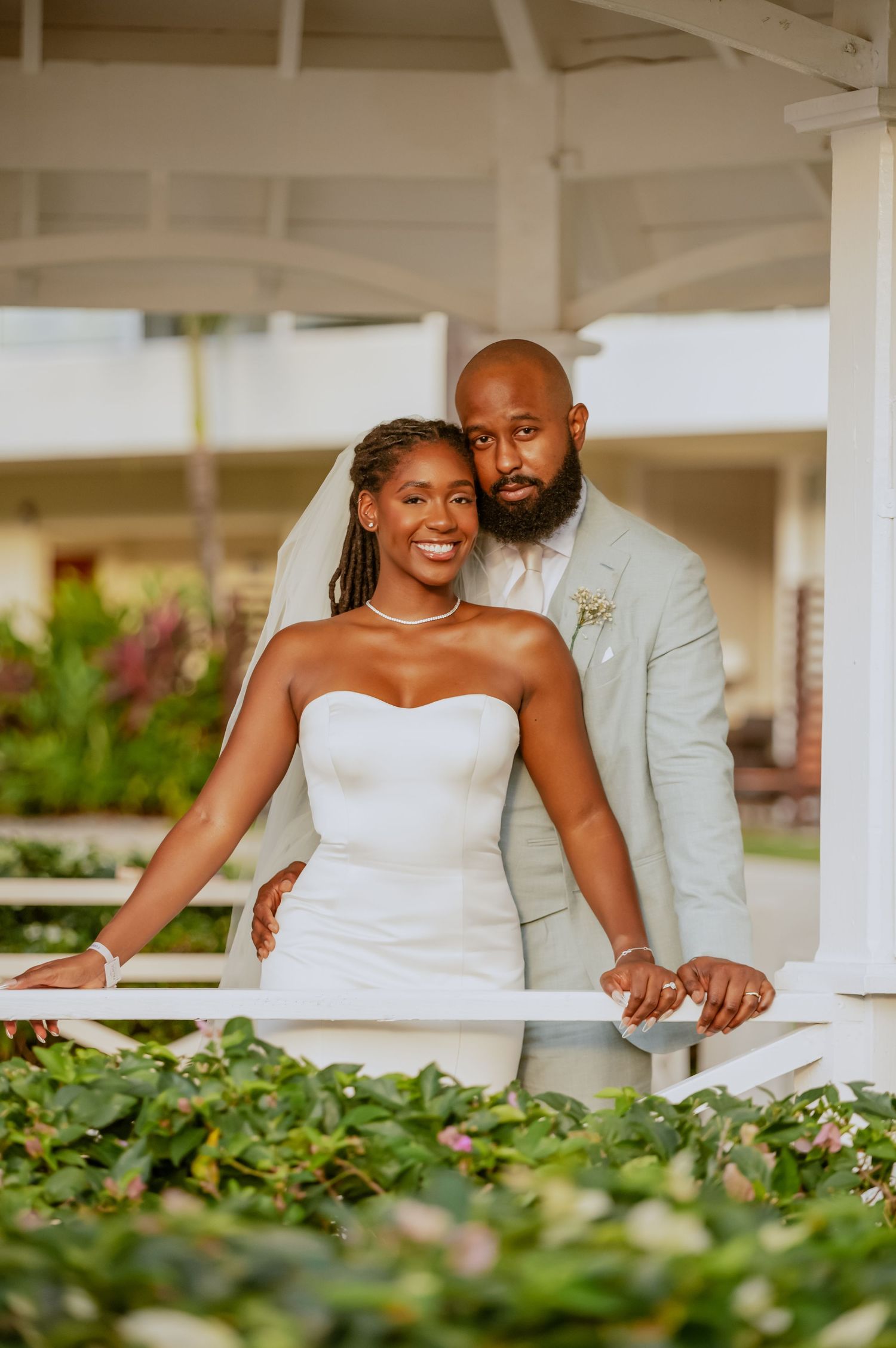 A relaxed wedding photoshoot under a covered porch with tropical plants in the foreground.