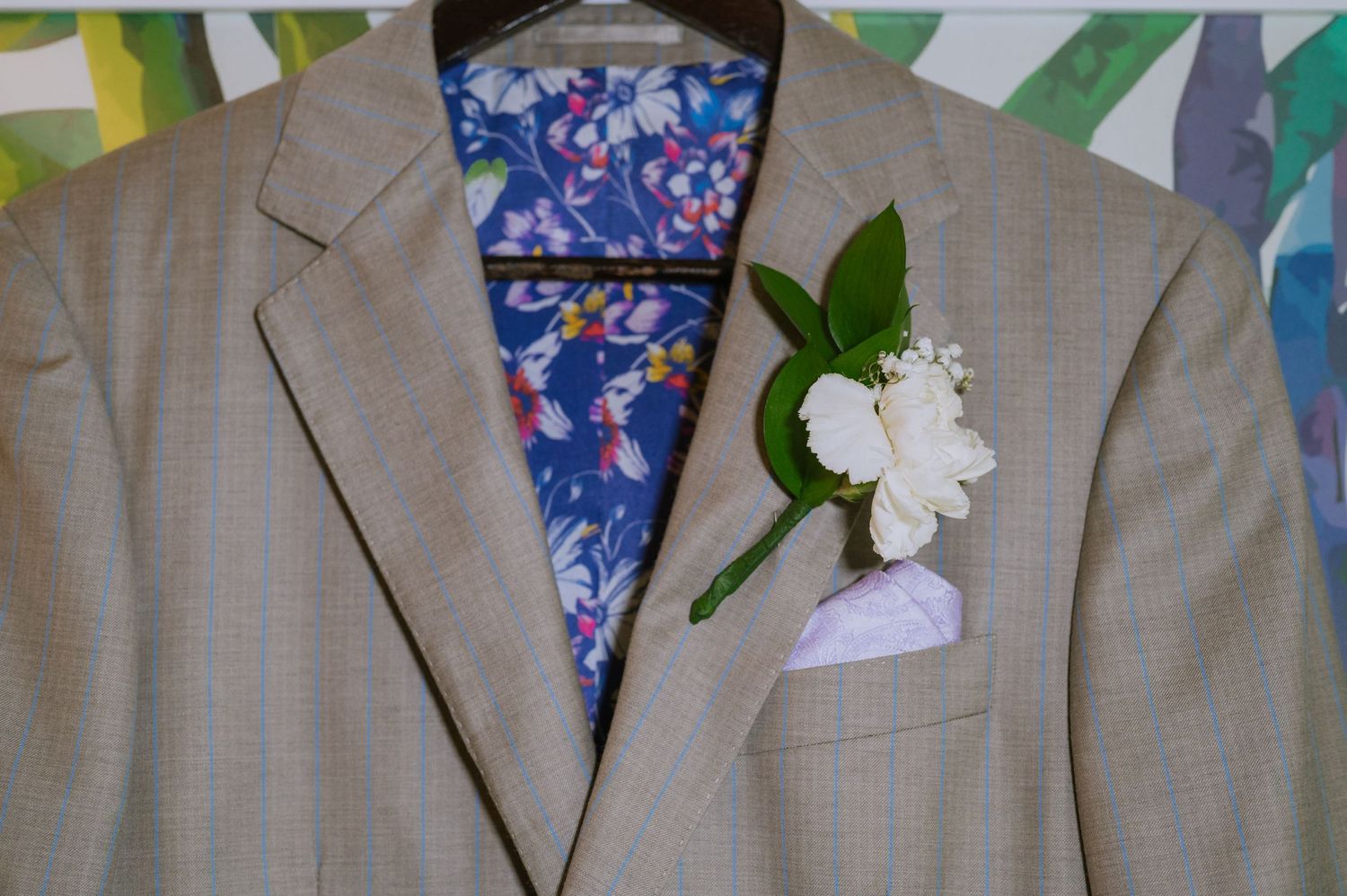 Light gray suit jacket with floral lining and white boutonniere displayed on hanger.