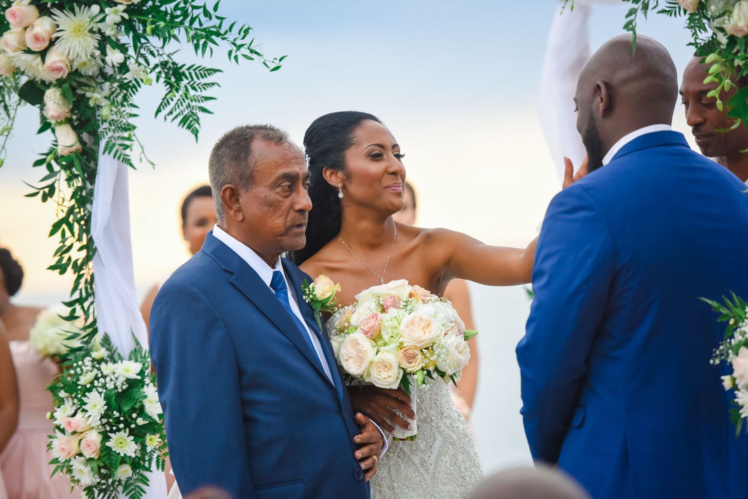Emotional wedding ceremony exchange under floral arch with white roses.