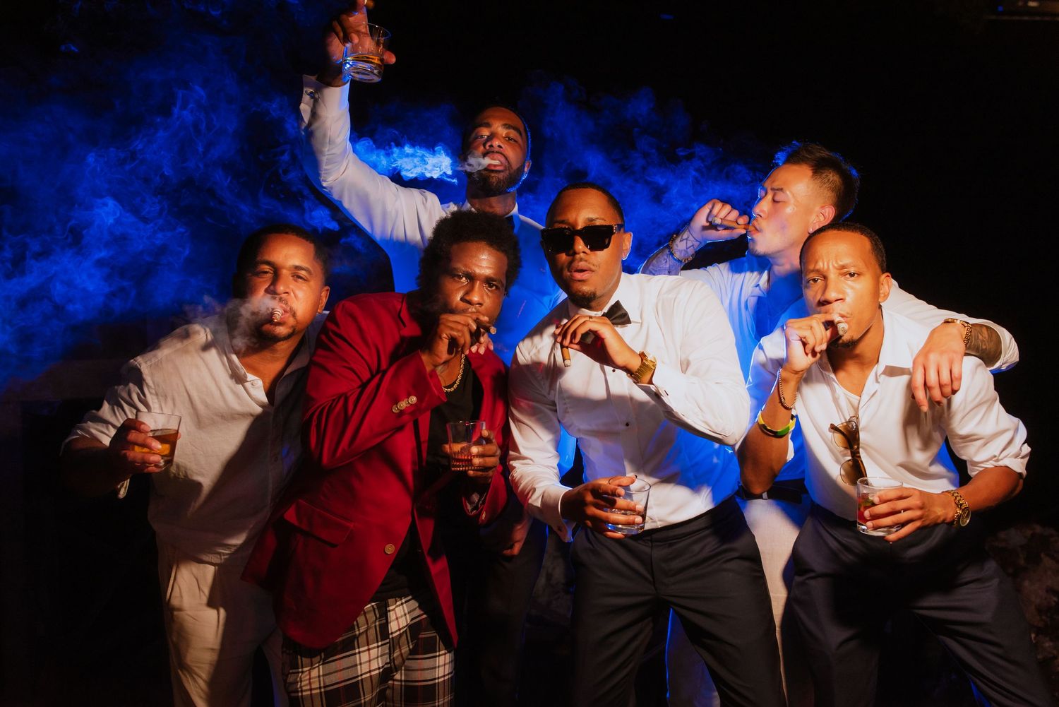 Group celebrates with drinks against dramatic blue smoke backdrop at nighttime party.