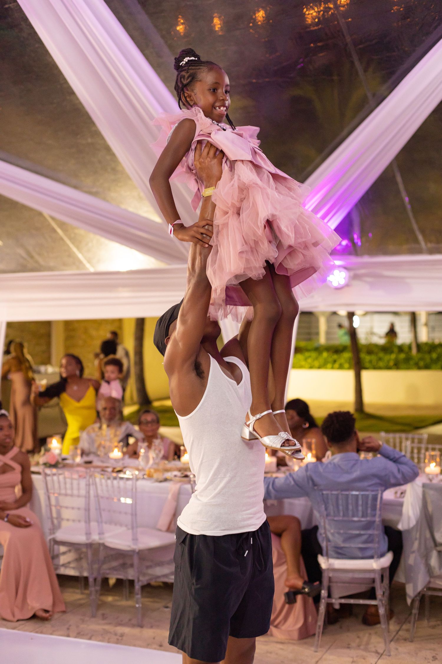 Wedding guests dance and celebrate under an elegant tent with purple accent lighting.