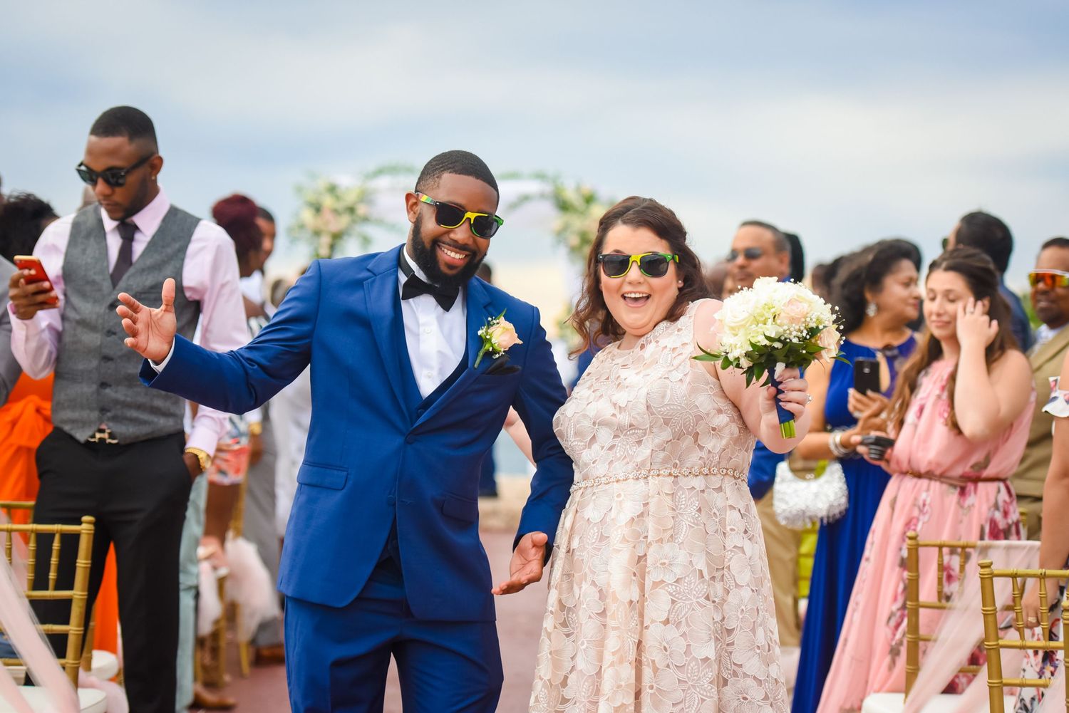 Wedding party and guests walking along beach pathway during daytime celebration.