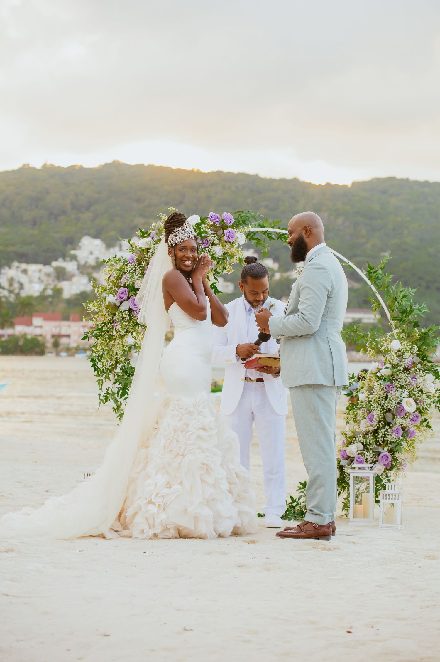 A romantic beach wedding ceremony with floral arch decorations and mountains in the background.