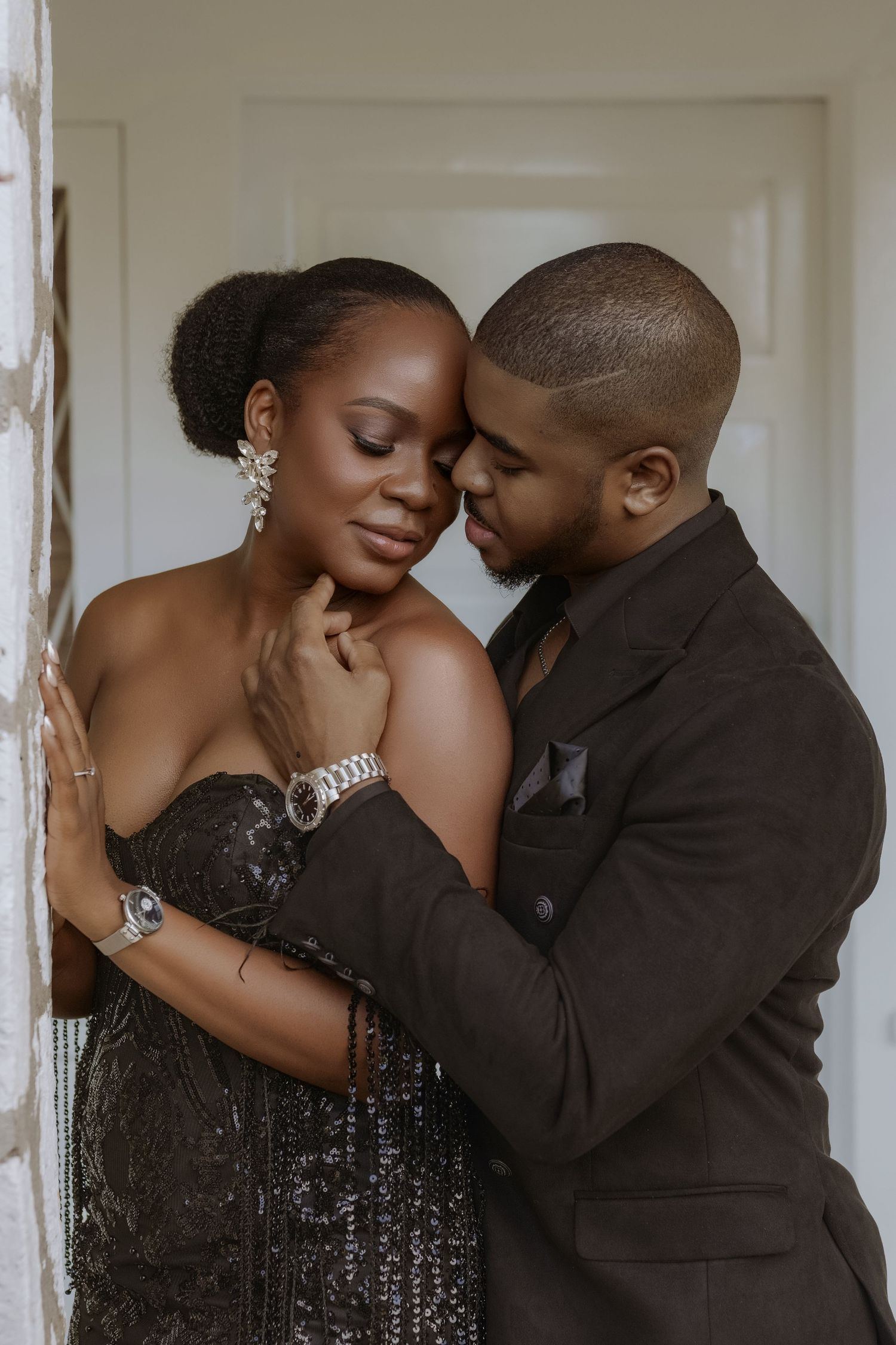 Romantic couple embracing in elegant formal attire against white interior backdrop.