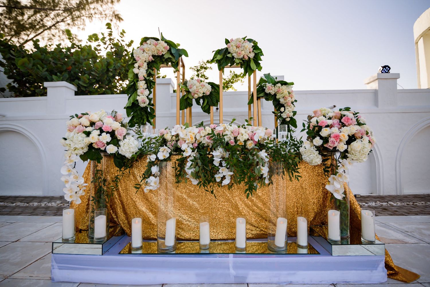 Luxurious head table decorated with cascading floral arrangements and gold sequin tablecloth.