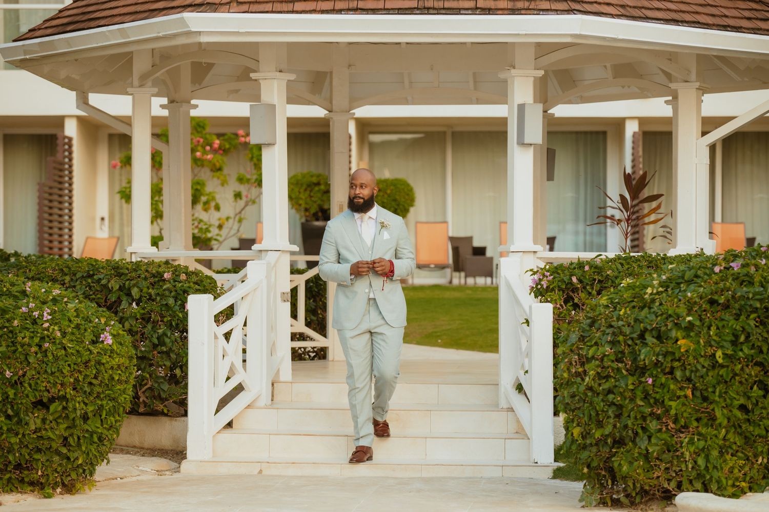 Elegant wedding party members walking along white columned porch in formal attire.