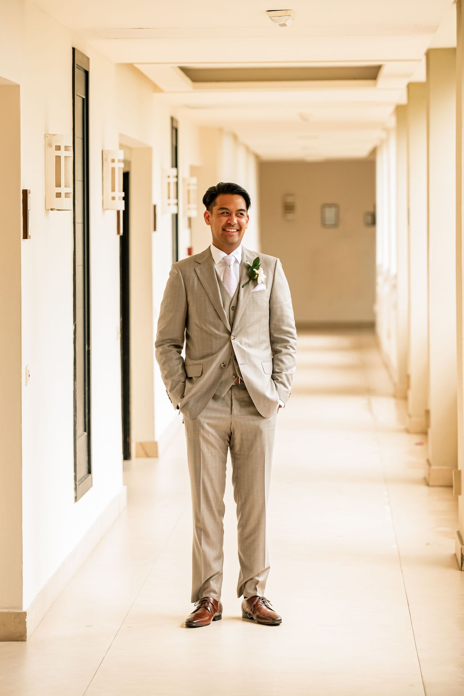 Groom in light grey suit standing in elegant hotel hallway.