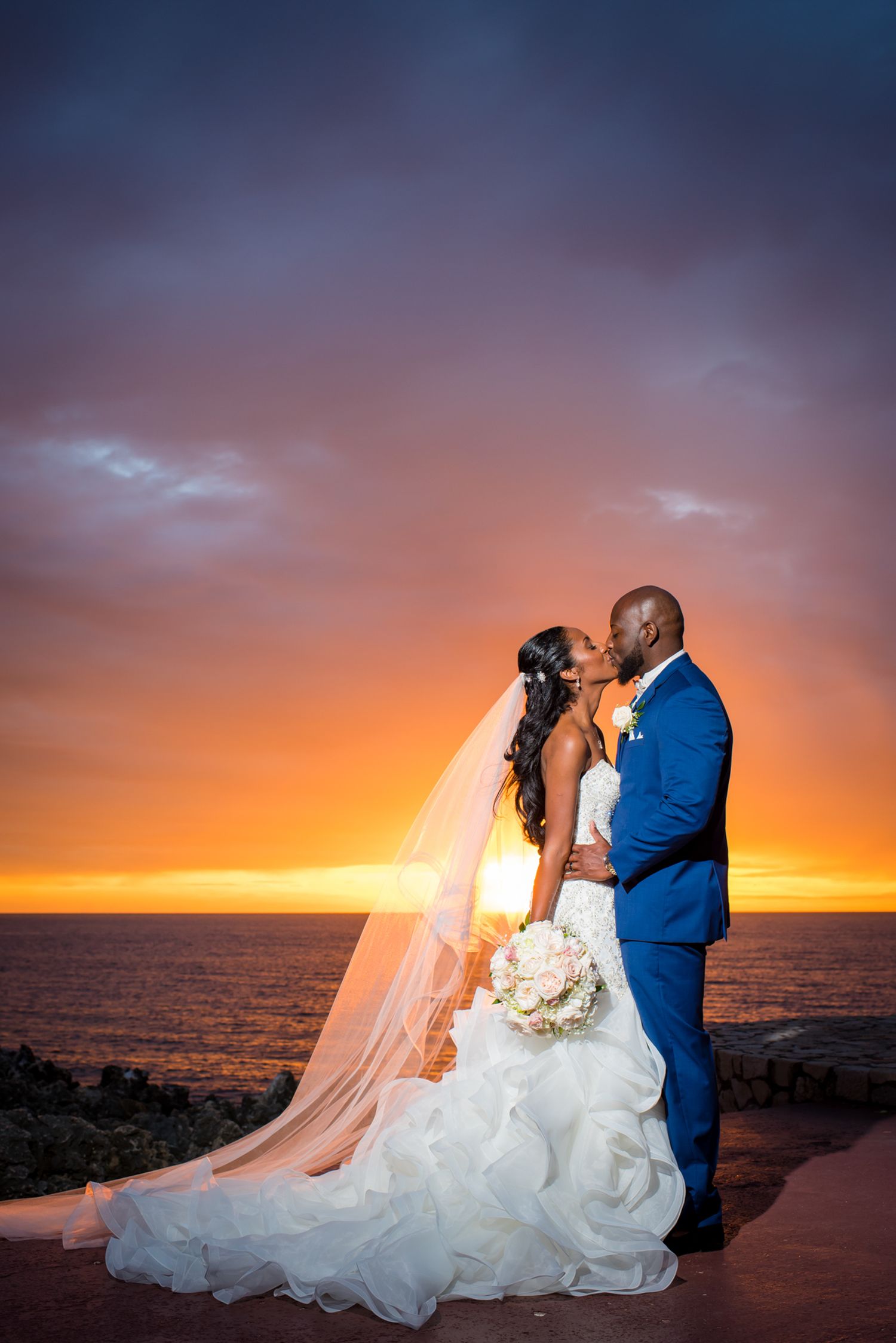 Romantic sunset silhouette of couple embracing against orange sky and ocean backdrop.