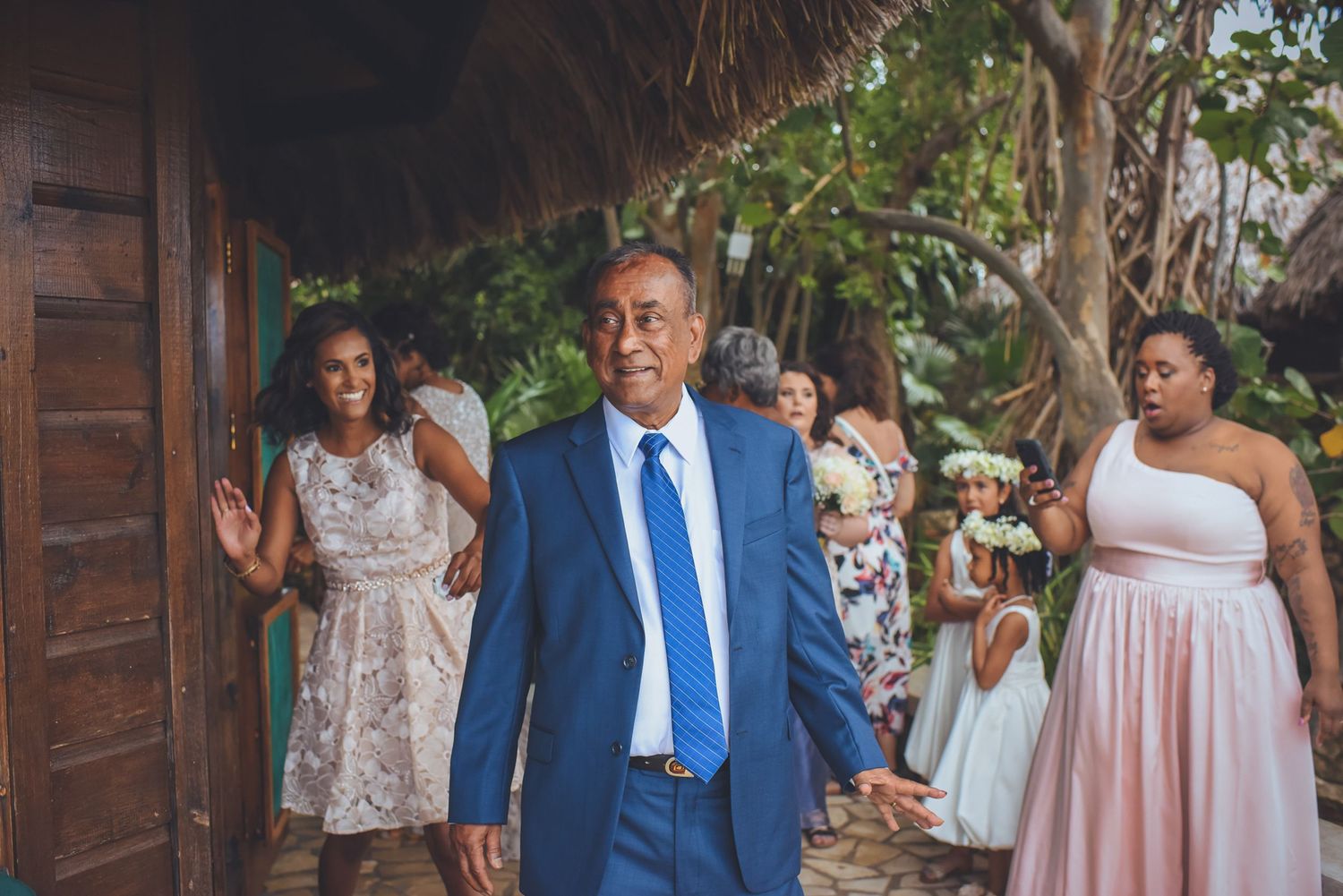 Wedding party members in pink dresses and blue suits gather outdoors for celebration photos.