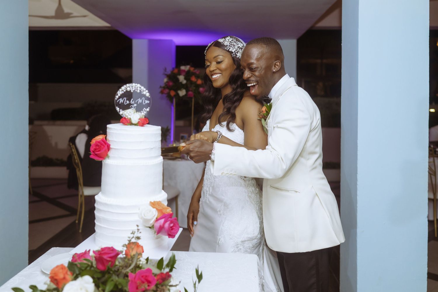 A wedding couple dances together at their reception while guests look on in an elegant venue with purple lighting.