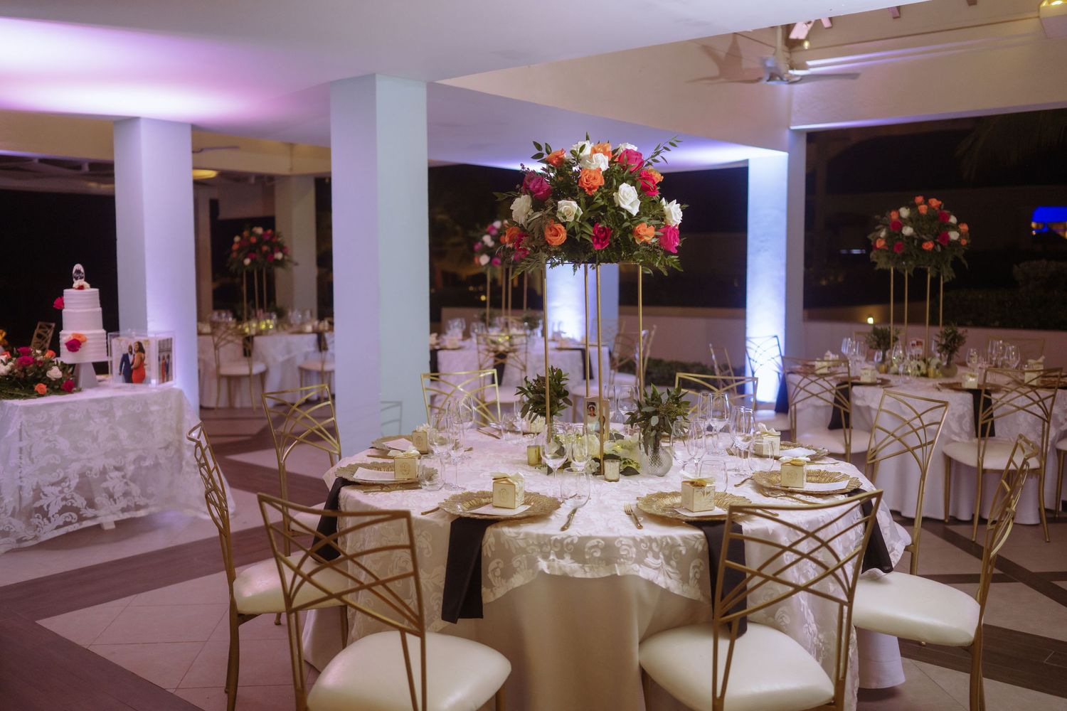 Elegant wedding reception setup with round tables, gold chairs and tall floral centerpieces.
