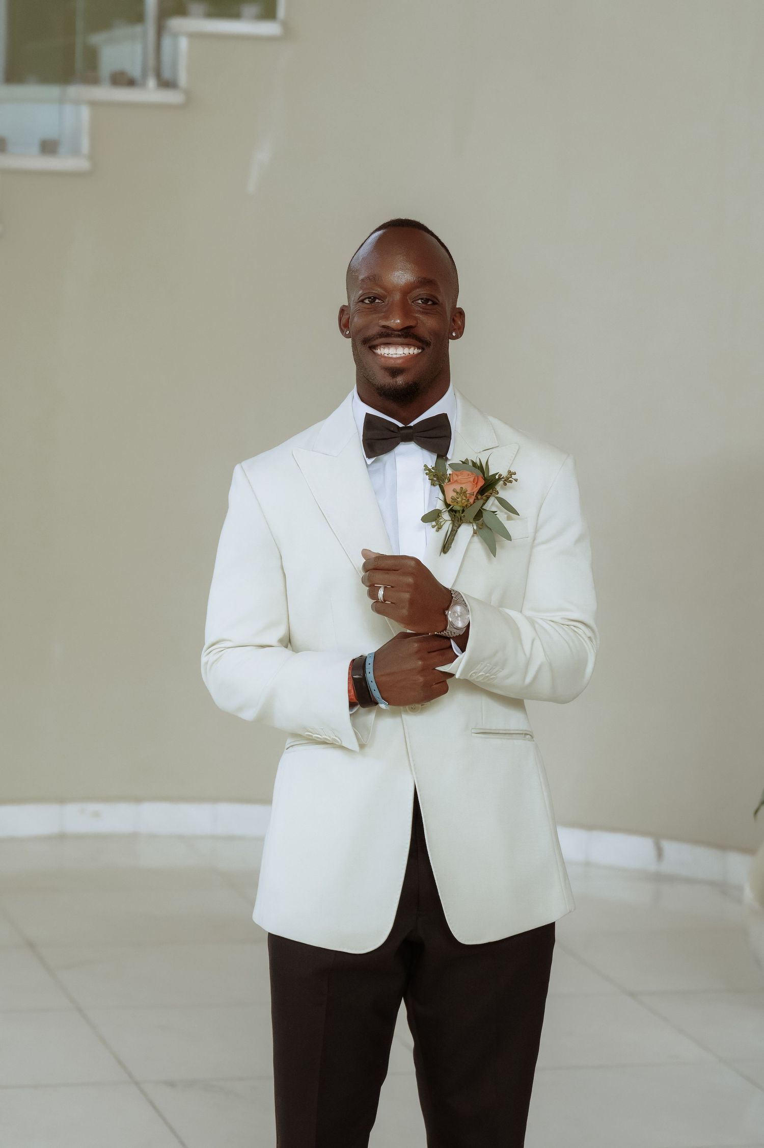A groom in a white tuxedo jacket and black pants poses for solo portraits.