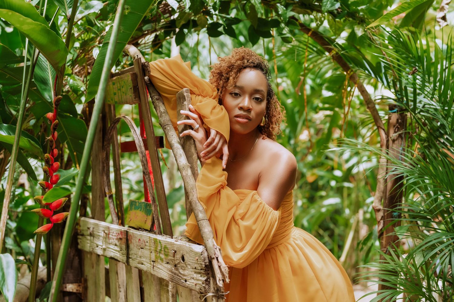 Artistic portrait in mustard yellow dress among tropical foliage and red flowers.