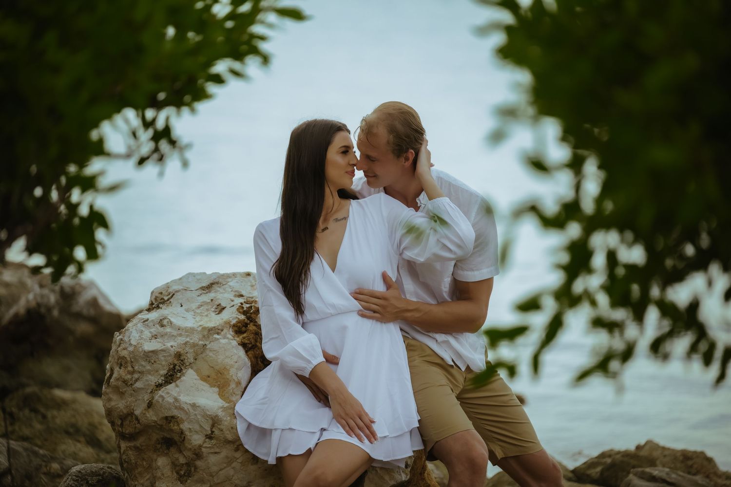 Couple shares tender moments during coastal photoshoot with ocean backdrop.