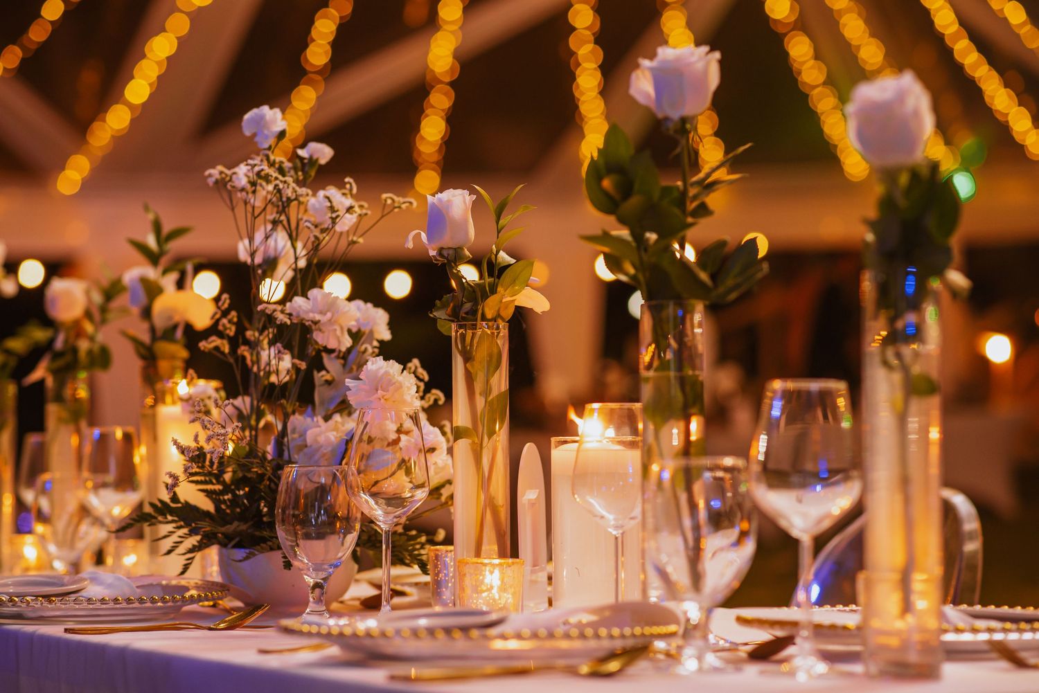 Wedding reception tables under golden string lights with floral centerpieces and candles.