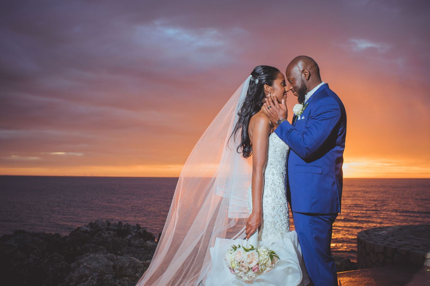 Romantic sunset beach wedding ceremony with flowing white fabric and floral decorations along the shoreline.
