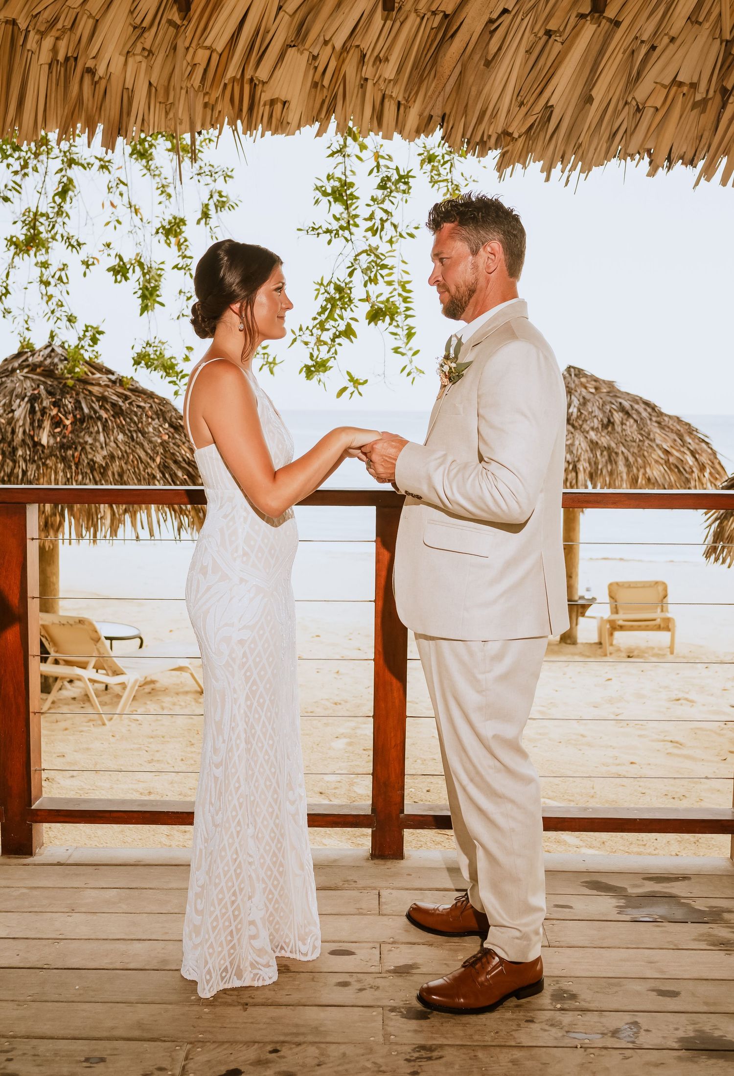 Wedding couple sharing intimate moments on a wooden deck with thatched roof and ocean views.