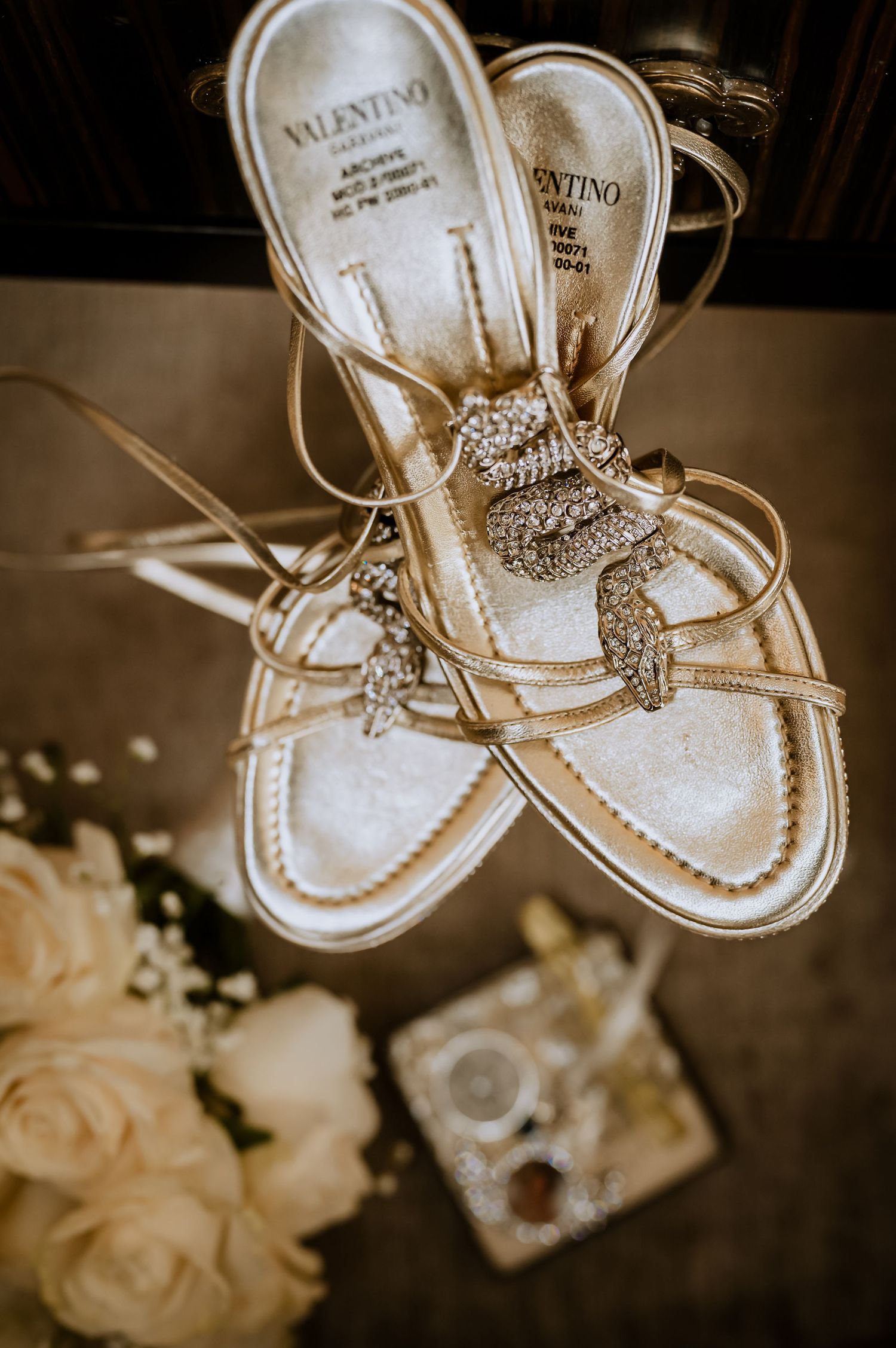 Valentino bridal sandals with crystal embellishments next to white roses.