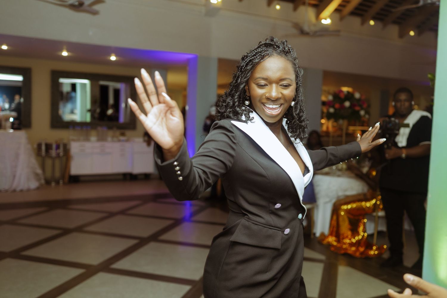 Wedding reception guests dancing and celebrating in an indoor venue with colorful lighting.