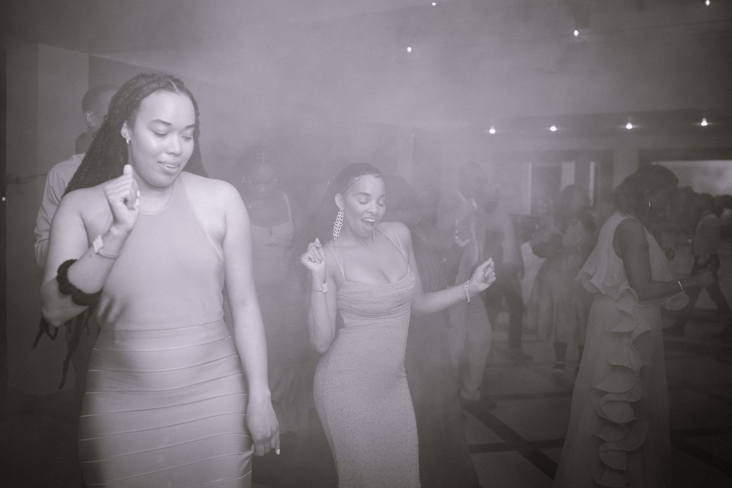 Wedding guests dance and celebrate in a dimly lit reception hall with a festive atmosphere.