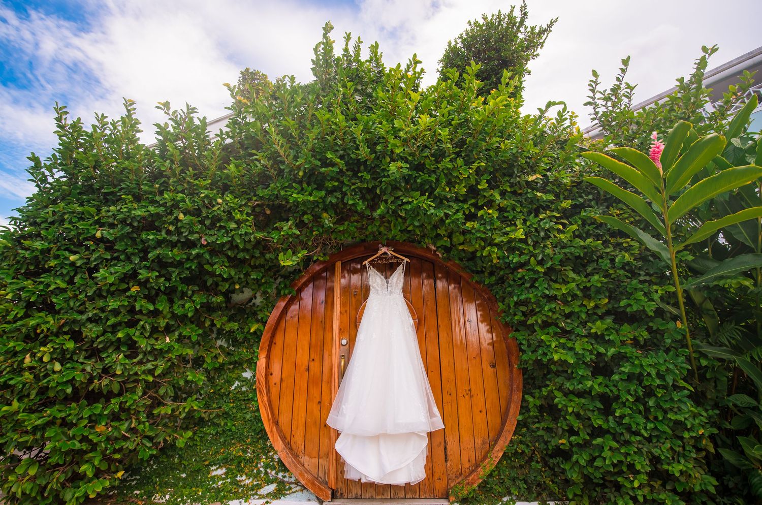 Wedding dress displayed against wooden circular backdrop with lush greenery.