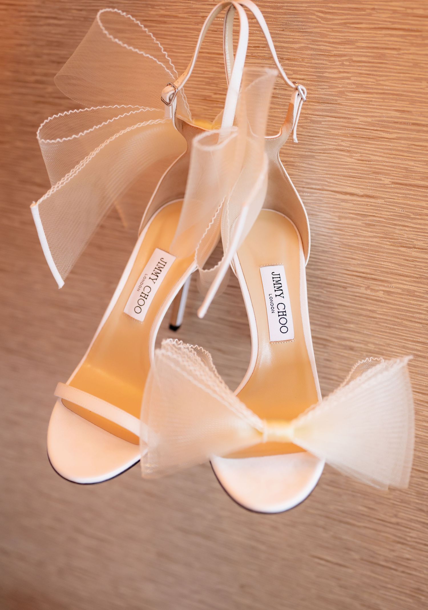 Elegant white bridal shoes with delicate straps displayed on wooden surface.