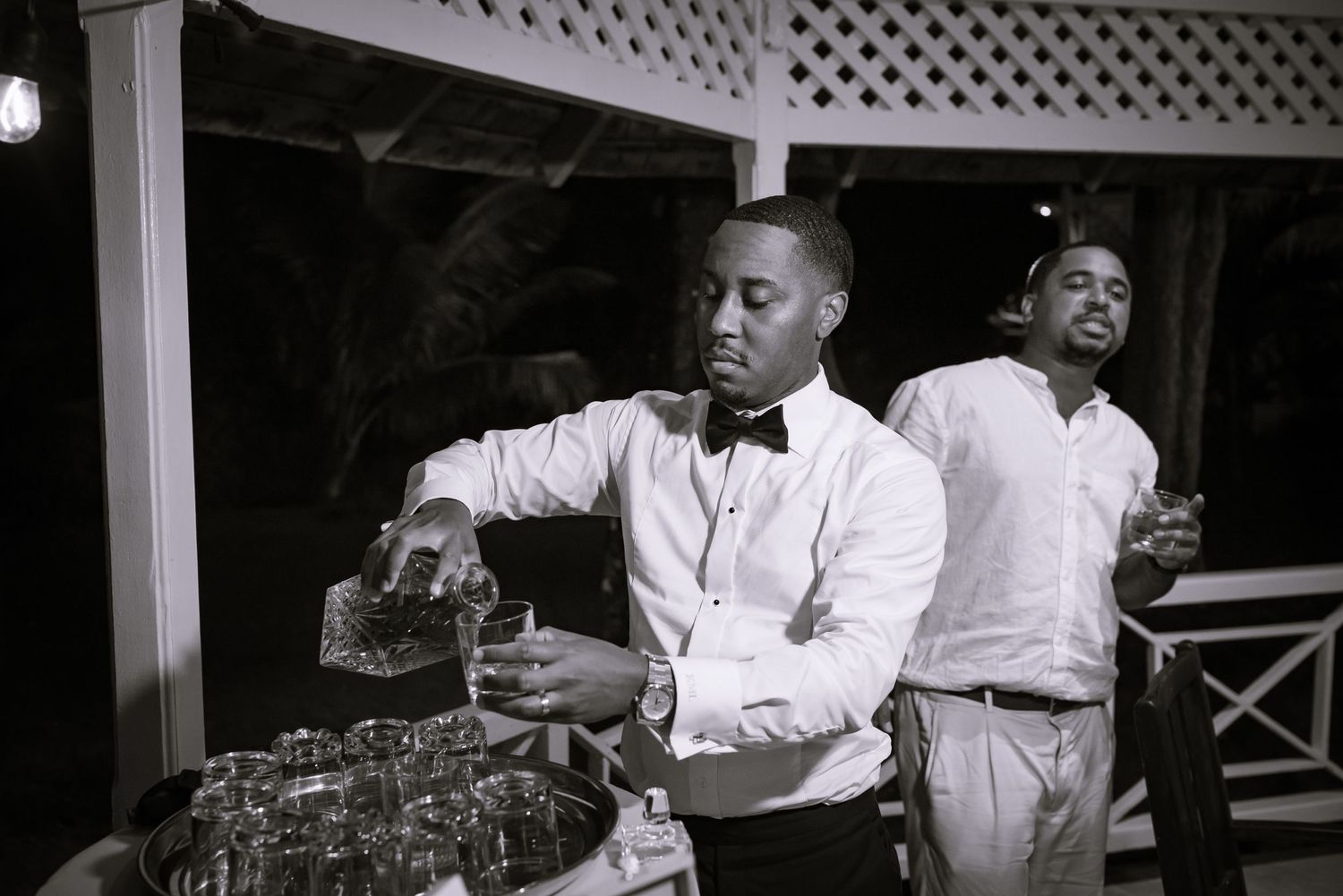 Bartender in formal attire pours drinks at elegant reception bar in black and white.