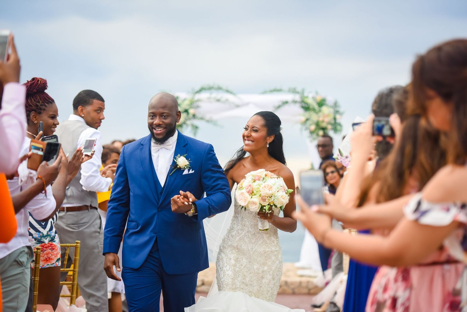Newlyweds exit their ceremony while guests capture the moment on their phones.