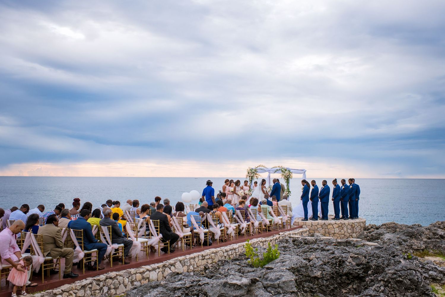 Scenic oceanside wedding ceremony setup with rows of white chairs on rocky cliff.