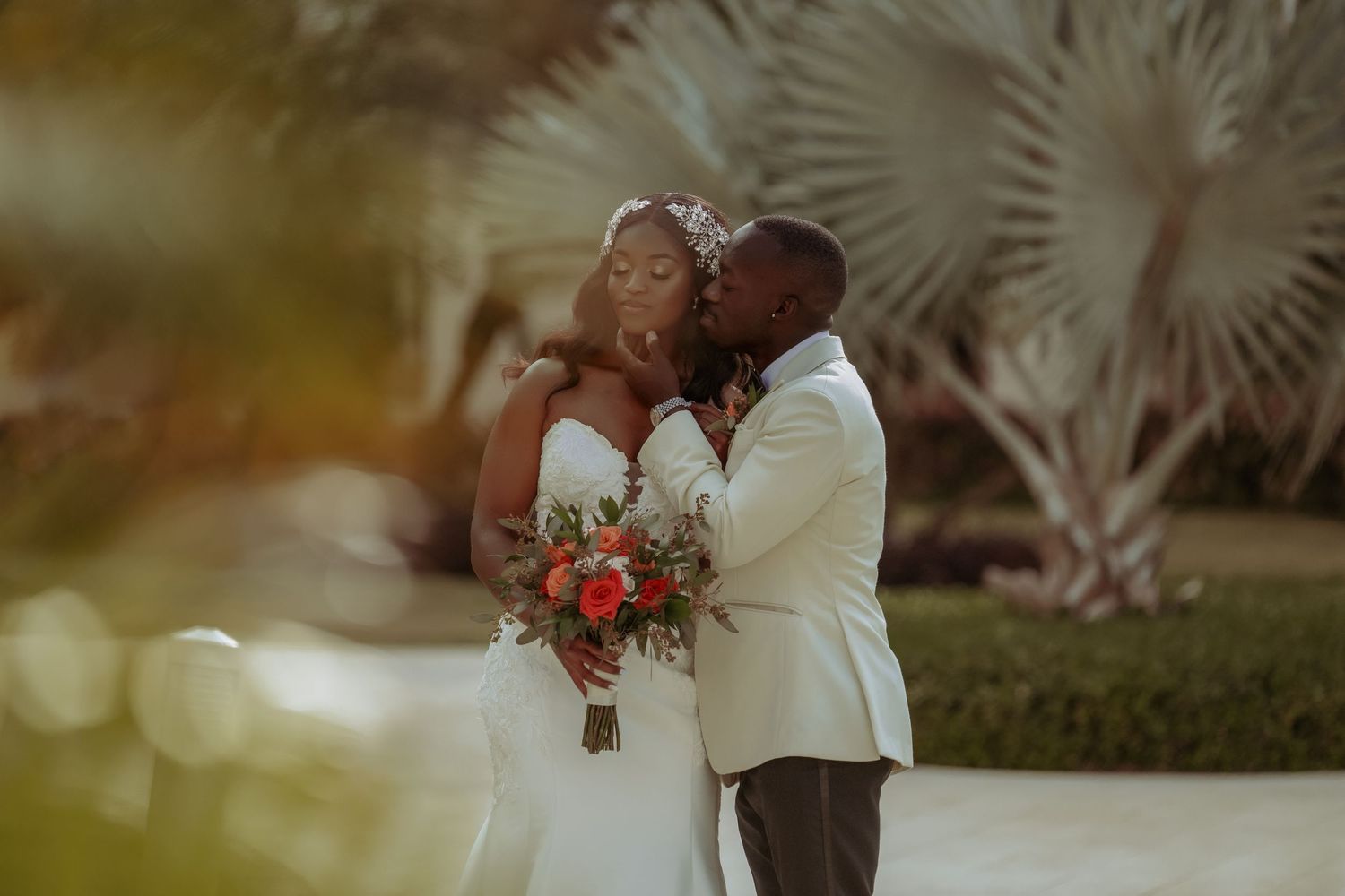 A romantic couple embraces in a lush garden setting during golden hour with palm trees in the background. Iberostar Montego Bay wedding