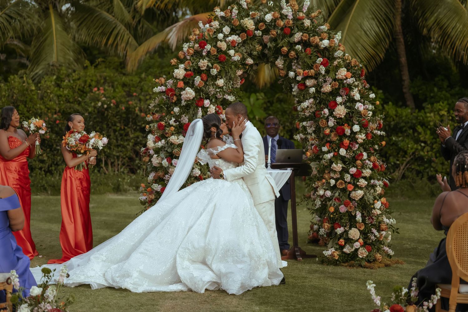 Outdoor wedding ceremony setup with floral arch and coral-colored decor under palm trees. Luxury wedding photography Half Moon Montego Bay
