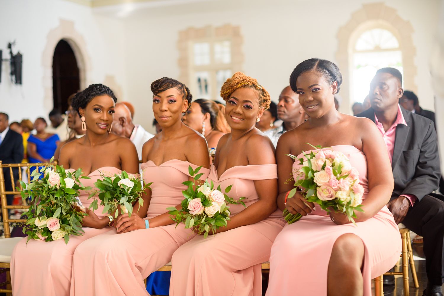 Bridesmaids in coral pink dresses pose together at formal wedding.