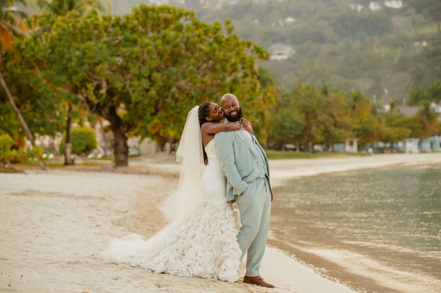 A romantic wedding portrait on a tropical beach with lush greenery.