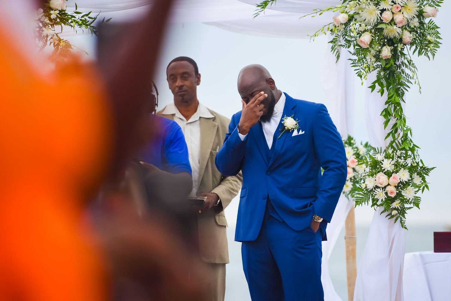 Wedding ceremony featuring groom in vibrant royal blue suit under floral archway.