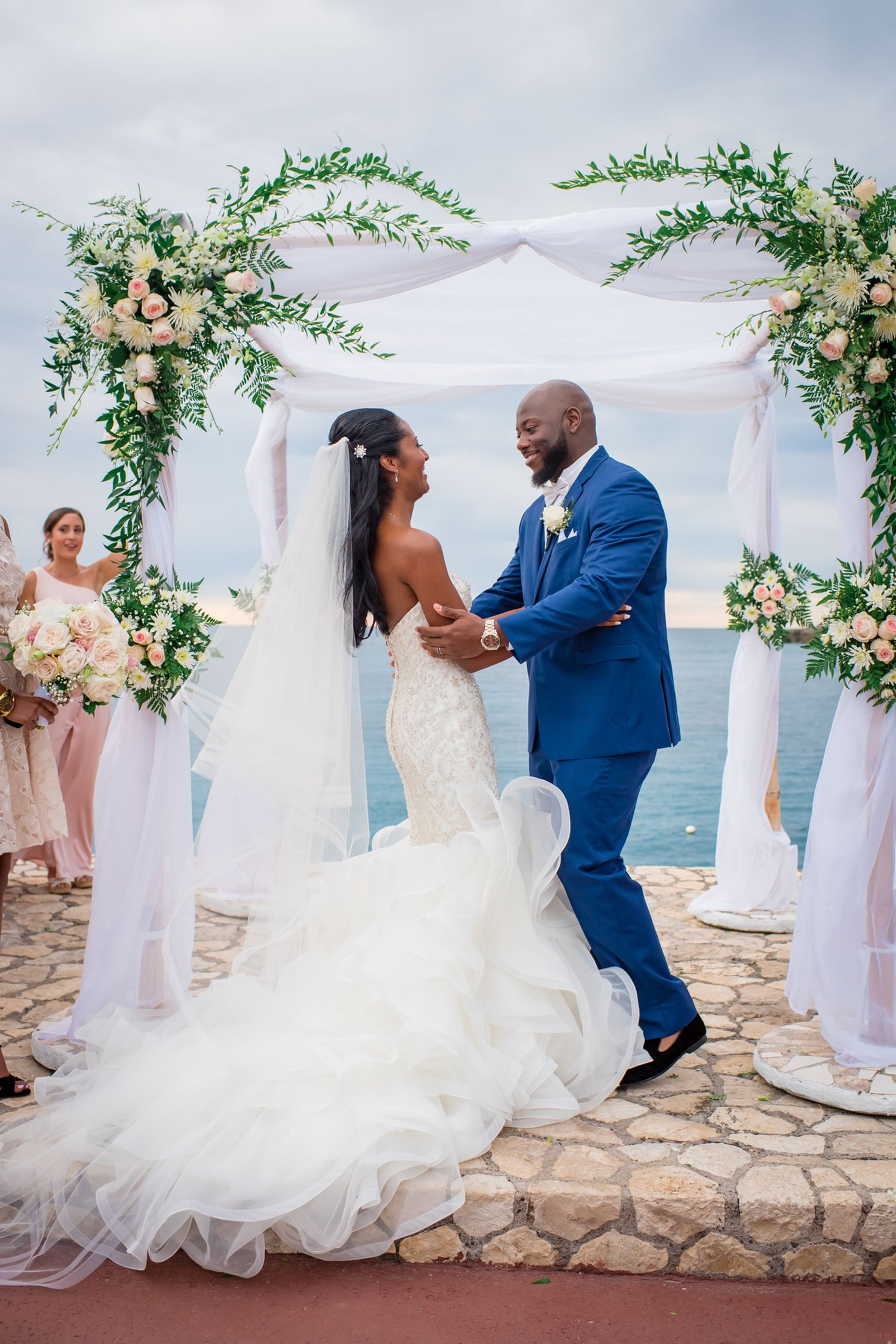 Elegant wedding ceremony on a stone terrace overlooking the ocean with white and floral decorations.