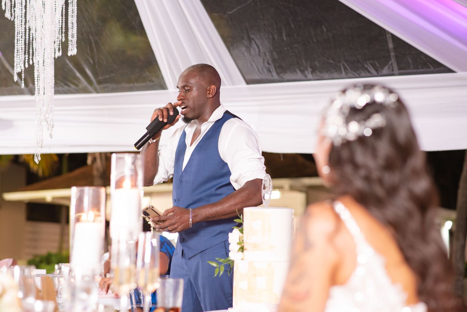 A wedding reception setup with elegant white draping and purple uplighting creates a romantic atmosphere.