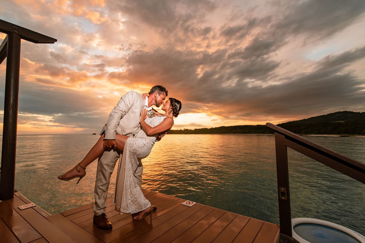 Romantic sunset wedding photoshoot on a wooden deck overlooking the ocean with dramatic clouds.
