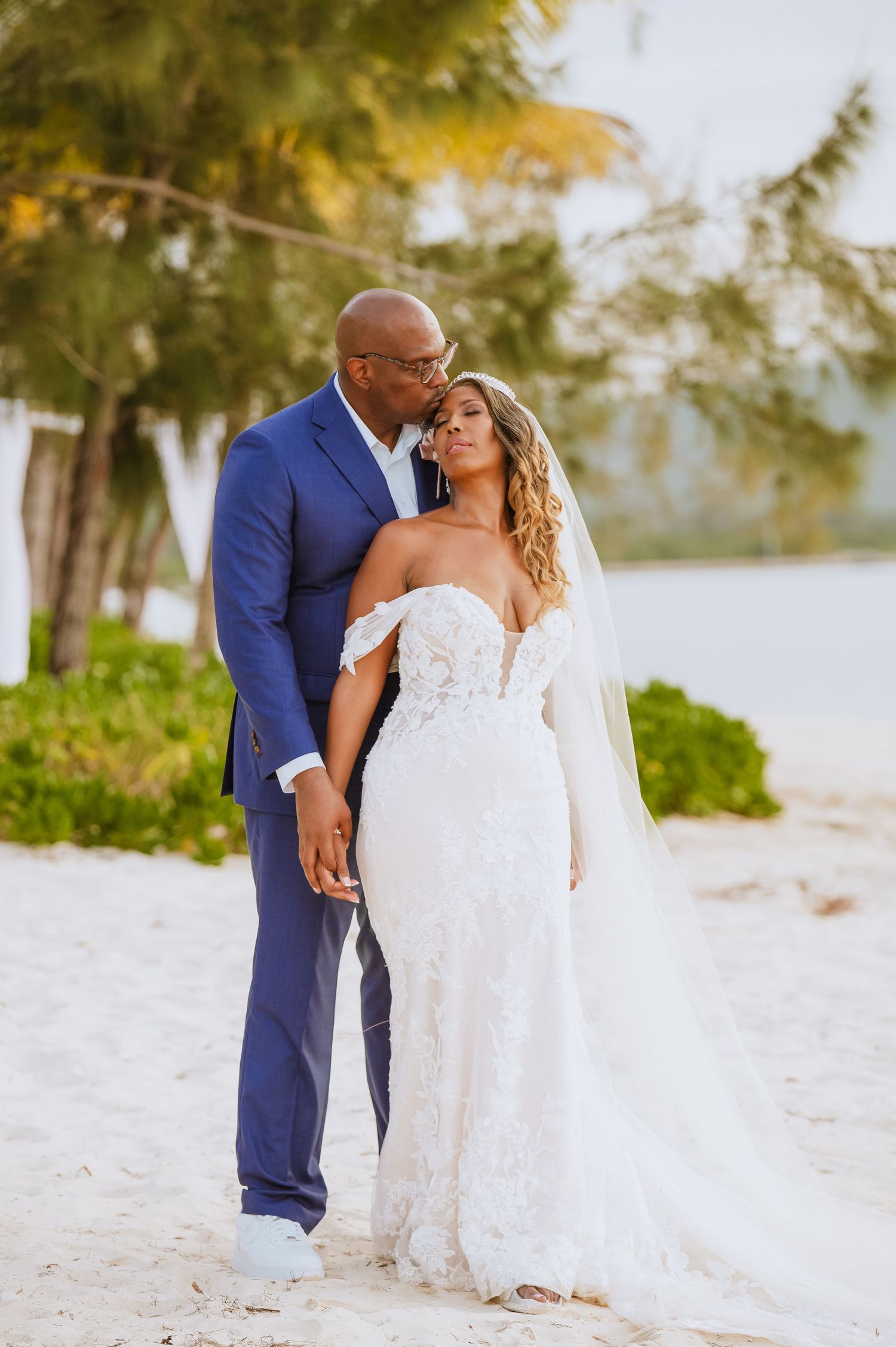Romantic beach wedding portraits with couple in white dress and navy suit on sandy shore.