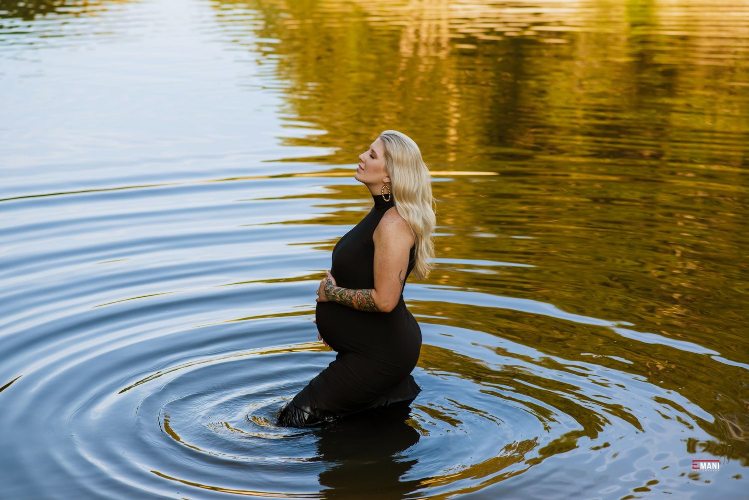 Woman in black dress stands peacefully in reflective water during golden hour.