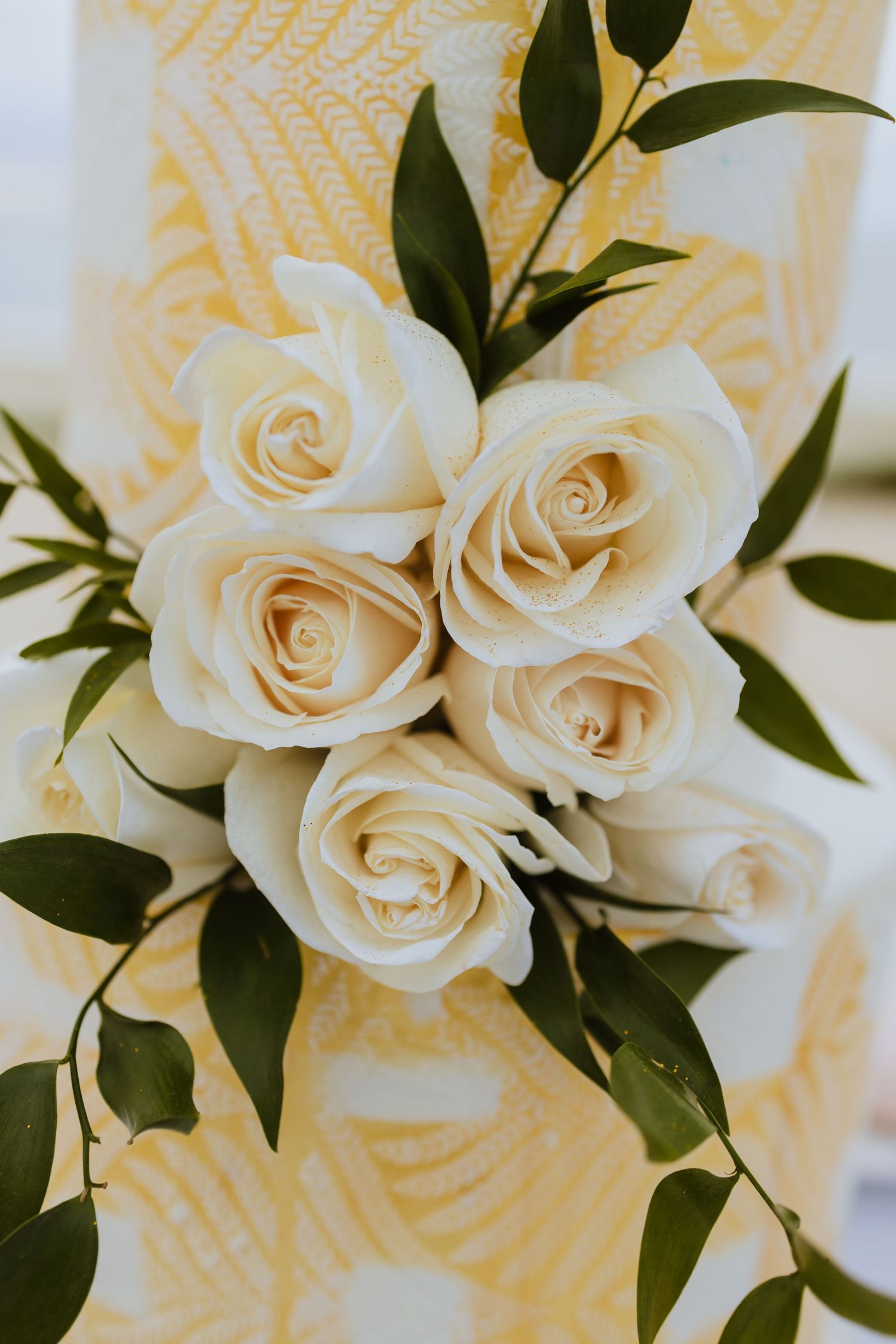 Close-up of cream-colored roses with green foliage against a textured background.
