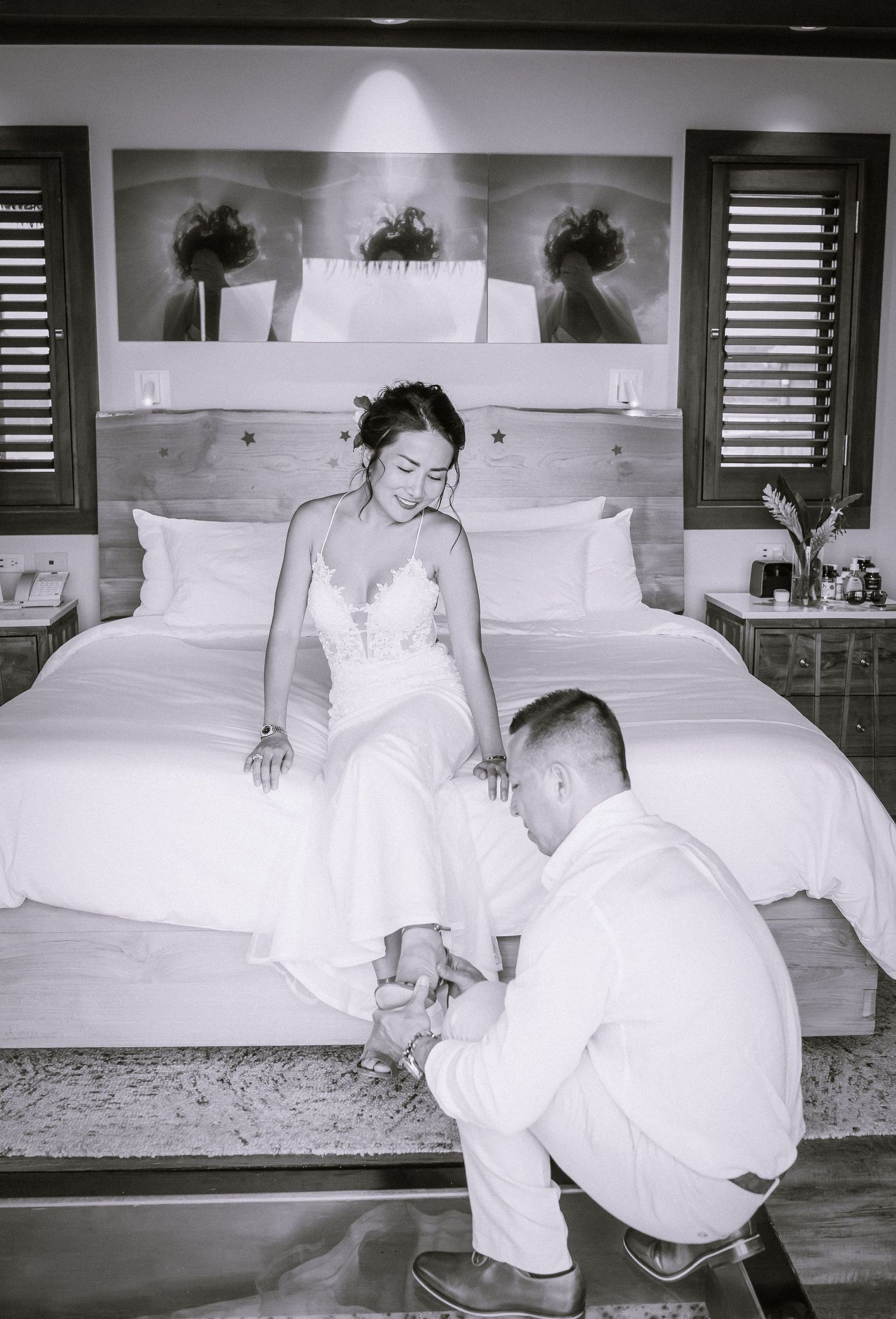 A couple shares playful moments on a white bed in black and white photography.