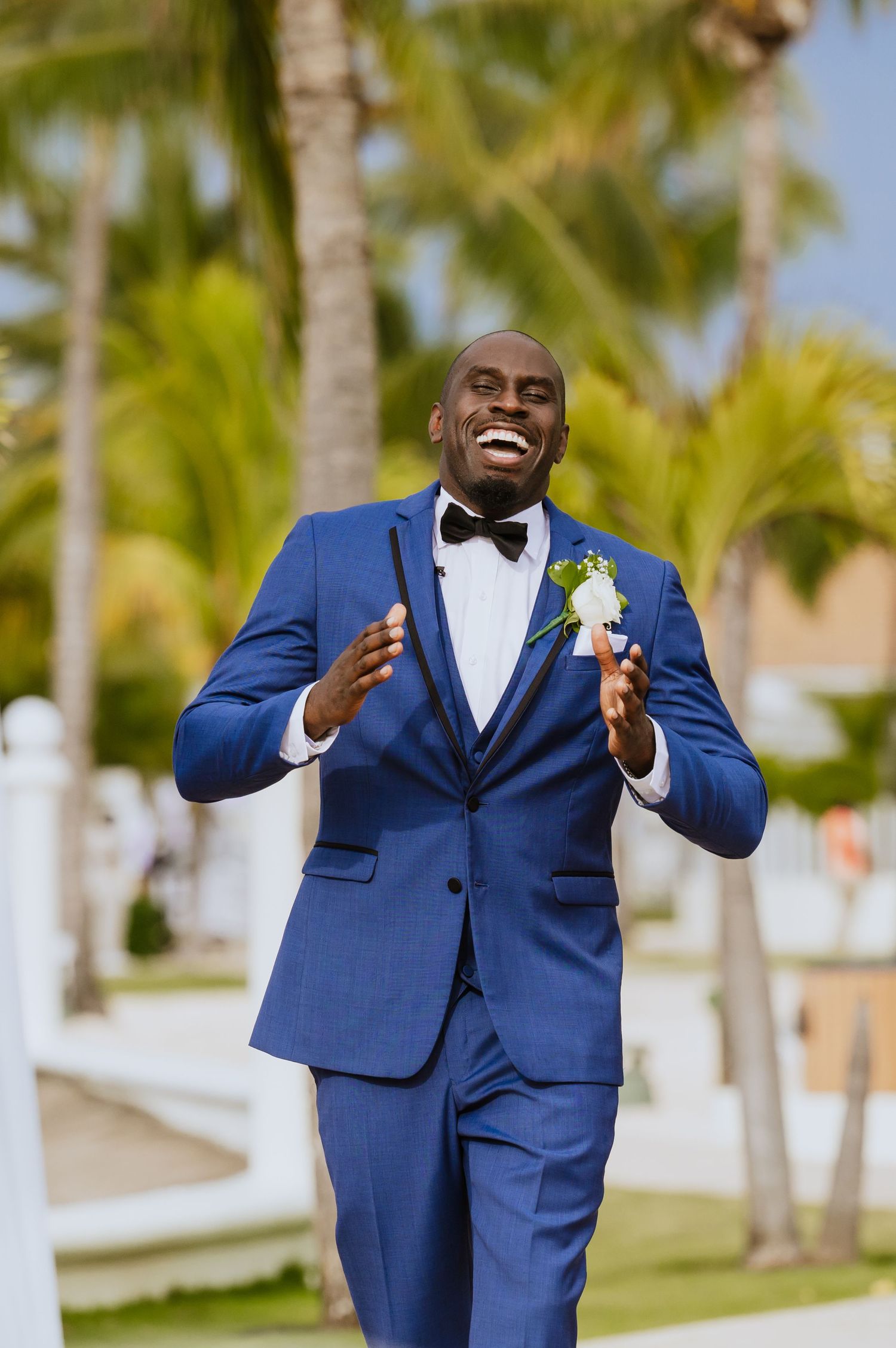 Groom in navy blue suit and bowtie shows joyful expressions during beach wedding.