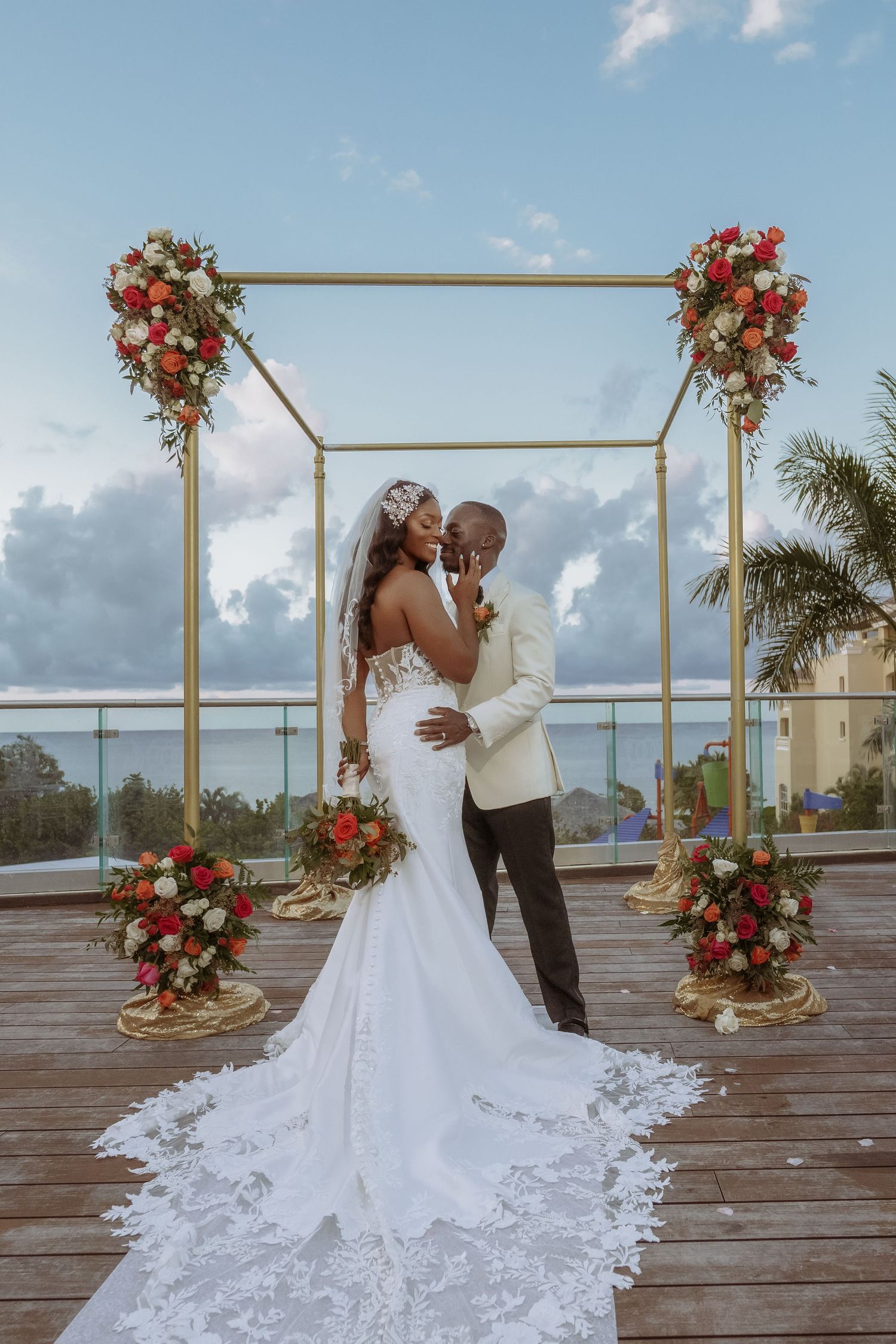 Wedding couple sharing intimate moment under gold arch decorated with red flowers.