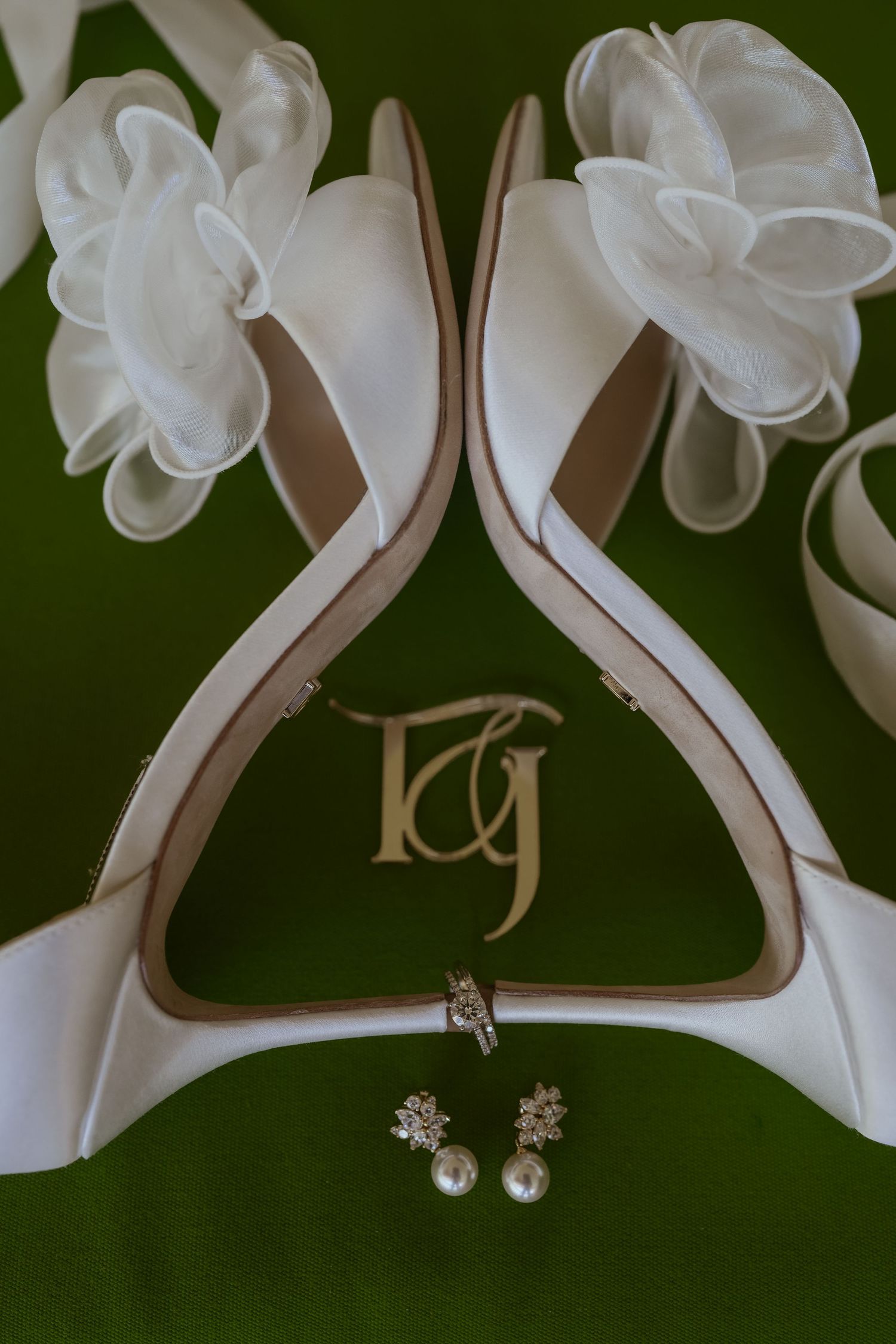 Wedding accessories including white heels, jewelry, and delicate details arranged on a dark green background.