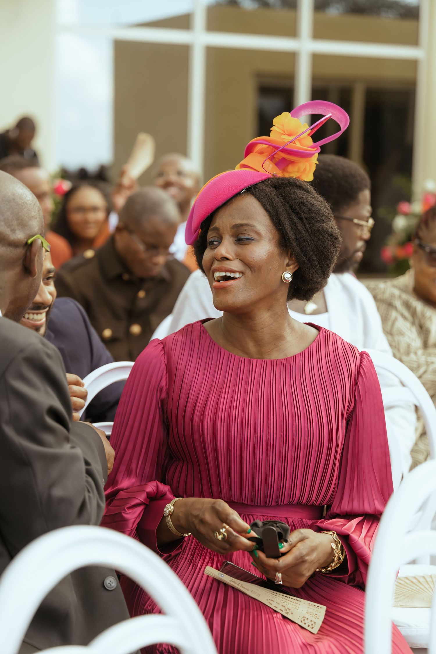 Guest in vibrant pink pleated dress enjoys festivities at wedding celebration.