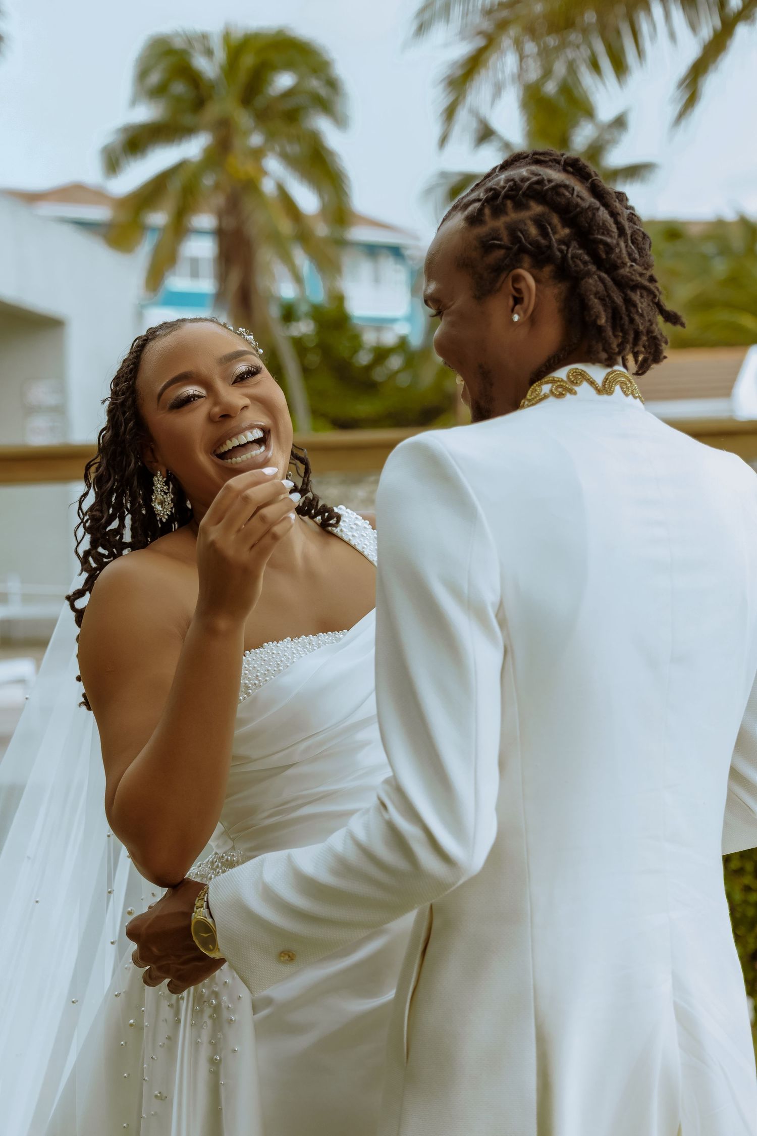 Joyful wedding couple embracing outdoors with palm trees in the background.