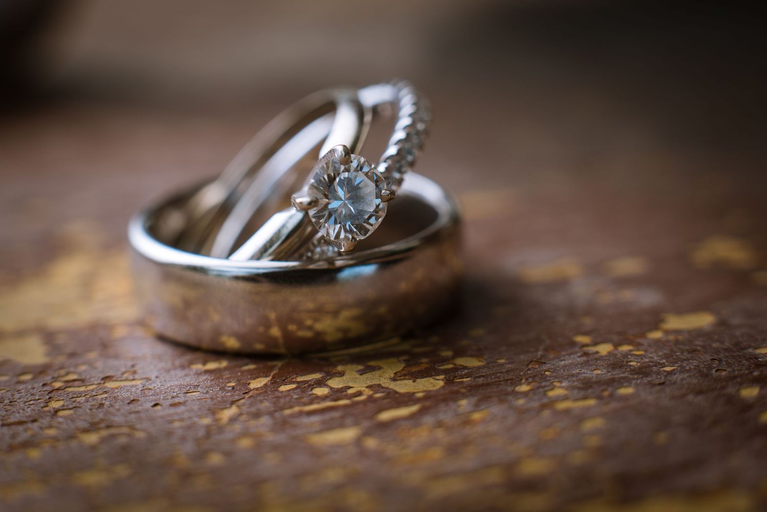 Detailed macro photography of diamond engagement ring and wedding band on brown surface.
